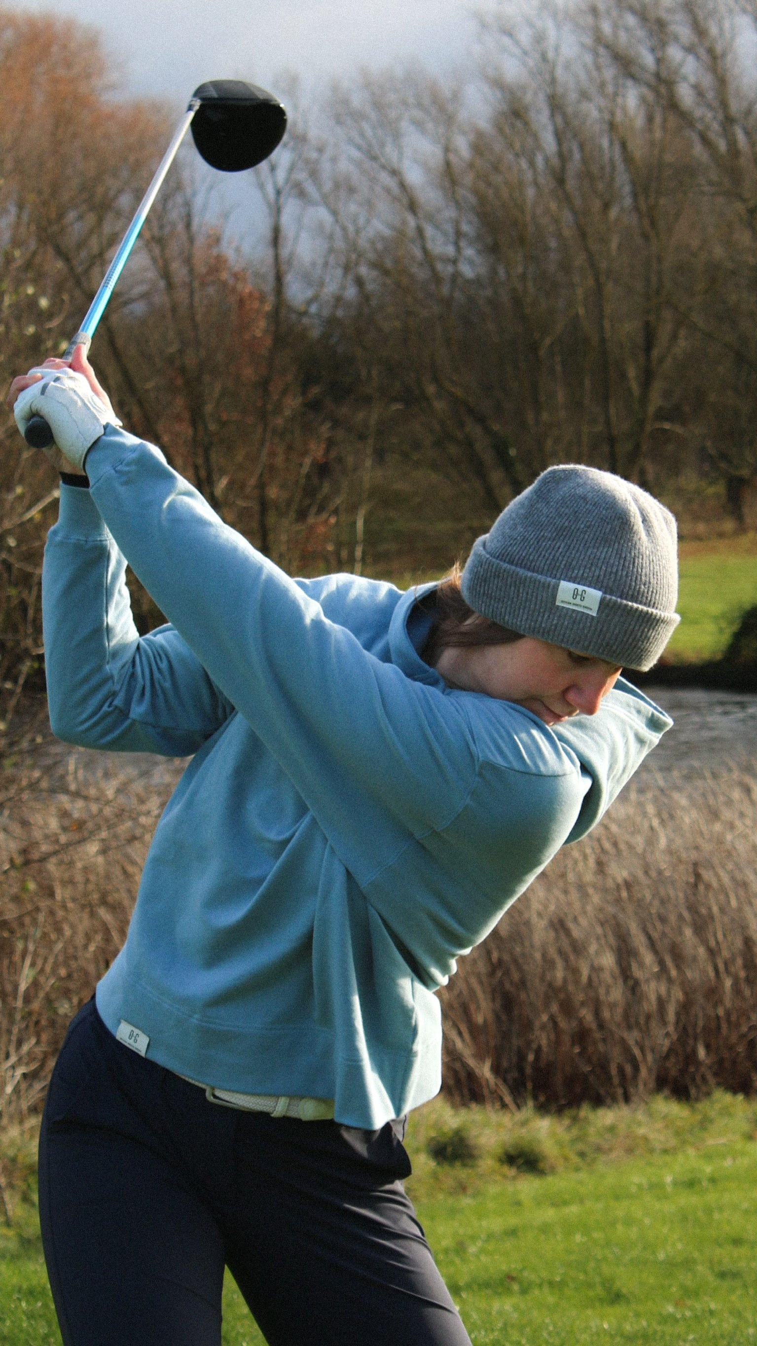 Ocean Meets Green Cloud beanie in grey, fine rib, made from merino wool, worn by a female golfer hitting a teeshot