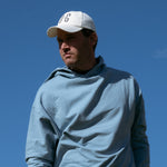 Ocean Meets Green Horizon cap in white with navy stitched logo, made from organic cotton, worn by a male golfer