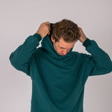Full body image of Ocean Meets Green men's golf hoodie Wave in pine, pulling the hood over the head
