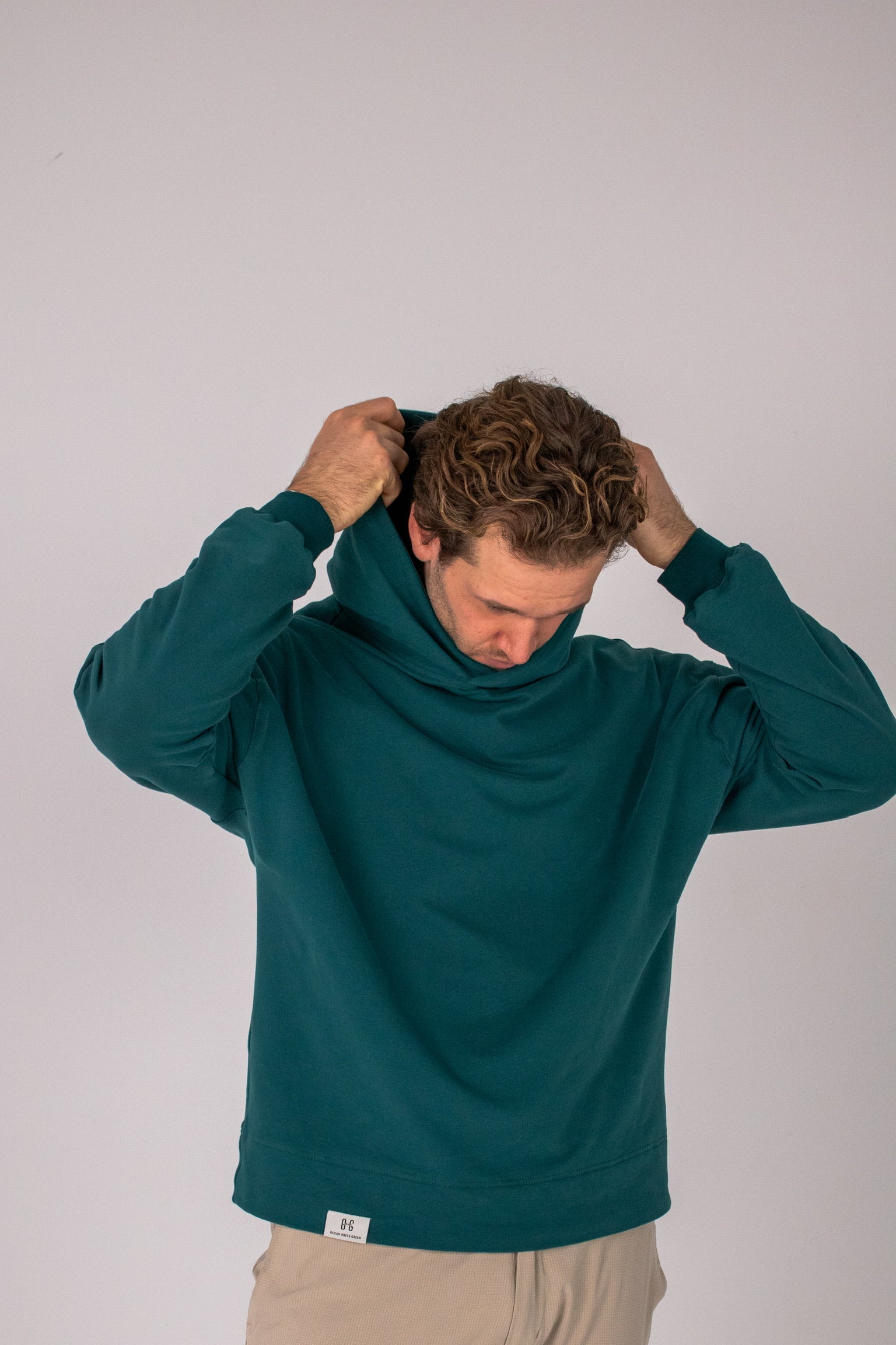Full body image of Ocean Meets Green men's golf hoodie Wave in pine, pulling the hood over the head