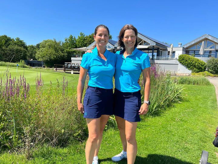 Image of two female golfers wearing the Ocean Meets Green TIDE skirt in navy and the MOANA poloshirt in light blue