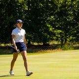 Image of female golfer wearing the Ocean Meets Green TIDE skirt in navy and the MOANA poloshirt in white