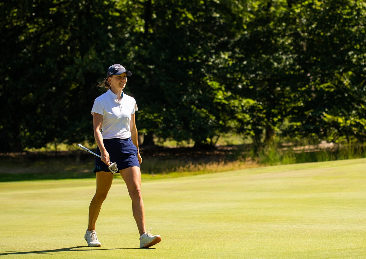 Image of female golfer wearing the Ocean Meets Green TIDE skirt in navy and the MOANA poloshirt in white