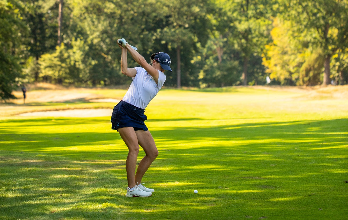 Image of female golfer wearing the Ocean Meets Green TIDE skirt in navy and the MOANA poloshirt in white