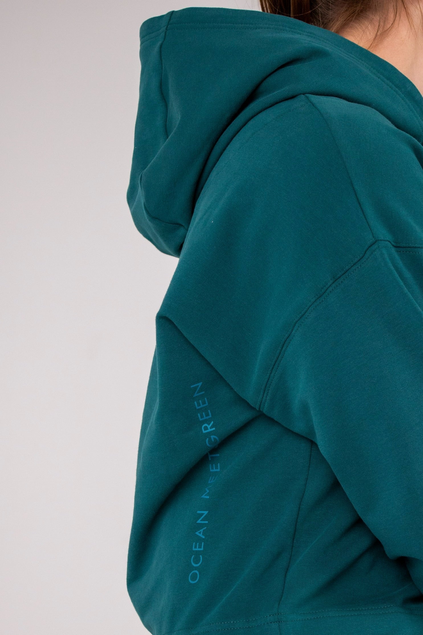 Closeup image of Ocean Meets Green women's golf hoodie Flow in pine, showing the logo