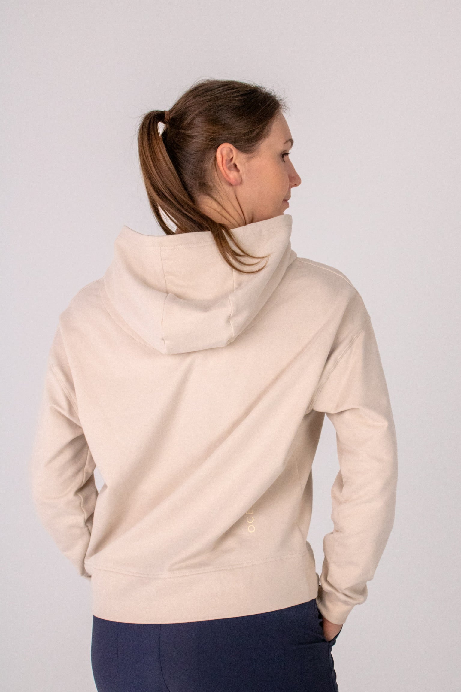Fullbody image of Ocean Meets Green women's golf hoodie Flow in sand, showing the back