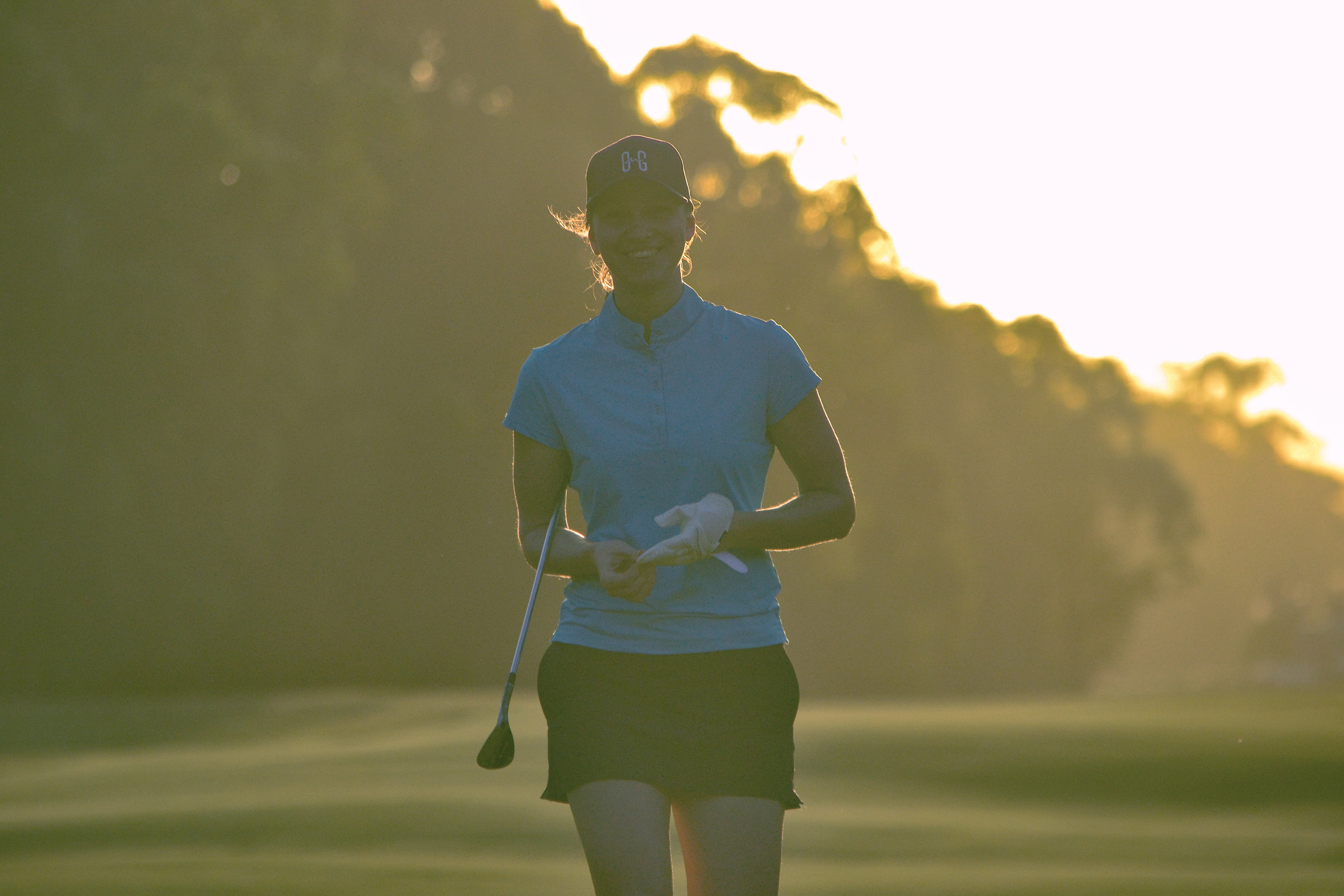 Image of woman wearing Ocean Meets Green Moana golf polo in light blue and Tide skirt in navy, walking onto the green
