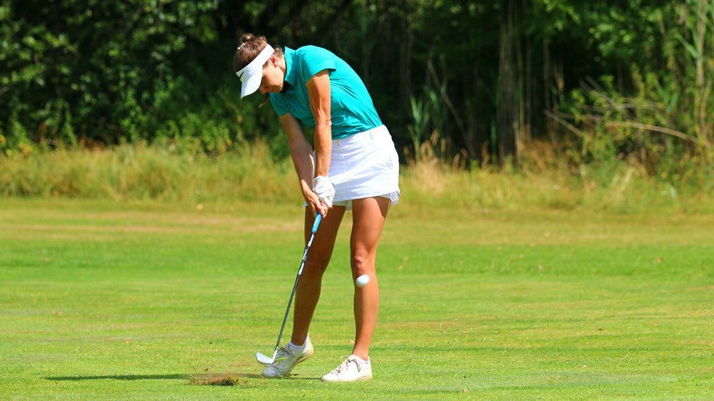 Image of female golfer wearing the Ocean Meets Green TIDE skirt in white and the MOANA poloshirt in green