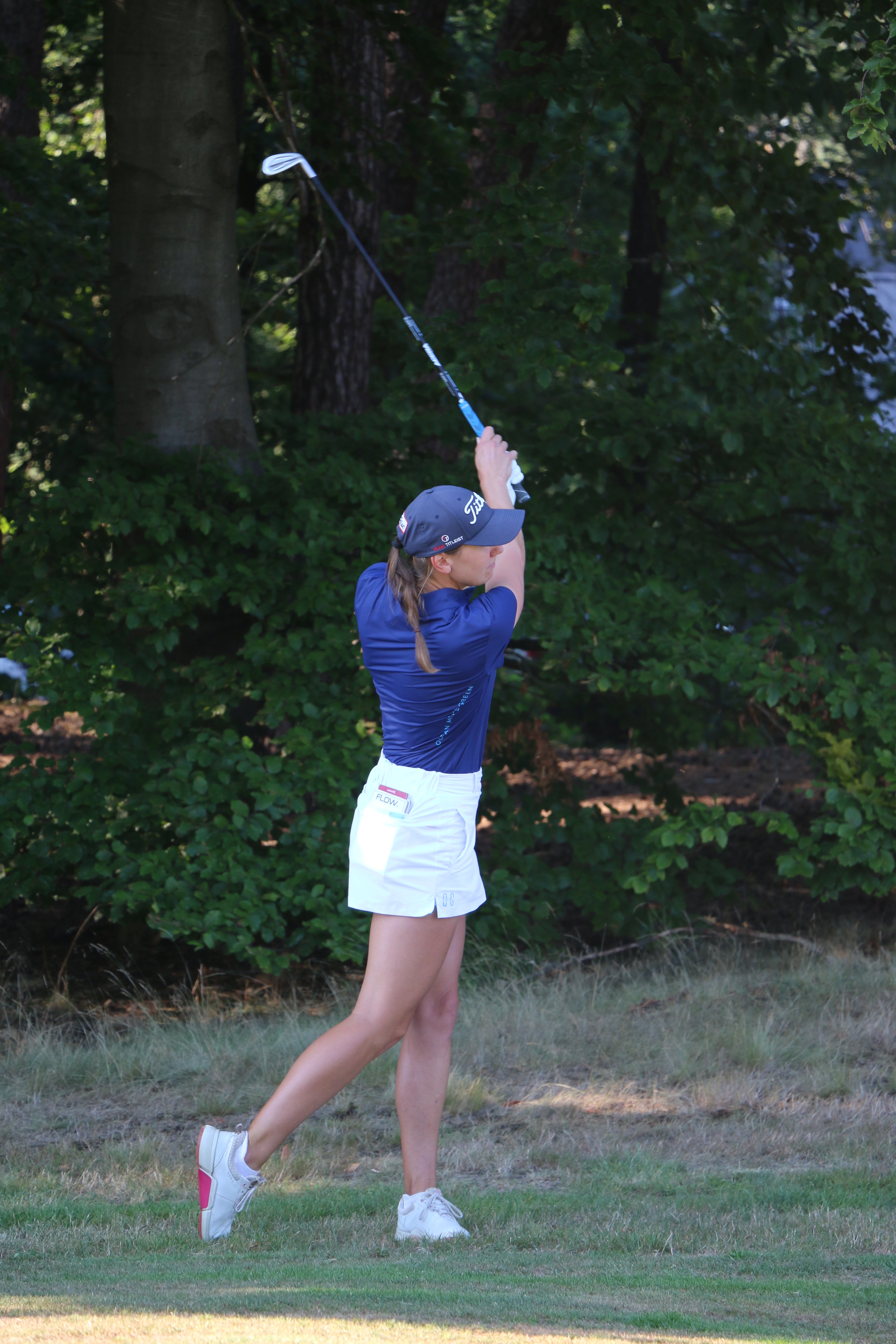 Image of woman wearing the Ocean Meets Green TIDE skirt in white and the MOANA poloshirt in navy