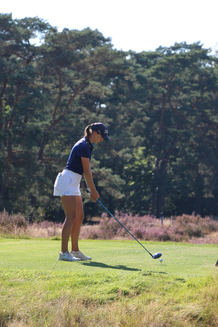 Image of woman wearing the Ocean Meets Green TIDE skirt in white and the MOANA poloshirt in navy