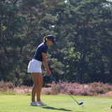 Image of woman wearing the Ocean Meets Green TIDE skirt in white and the MOANA poloshirt in navy