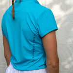 Full body image of Ocean Meets Green women's golf polo Moana in light blue worn by a woman, showing the side logo