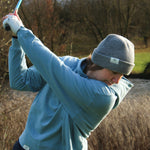 Ocean Meets Green Cloud beanie in grey, fine rib, made from merino wool, worn by a female golfer hitting a teeshot