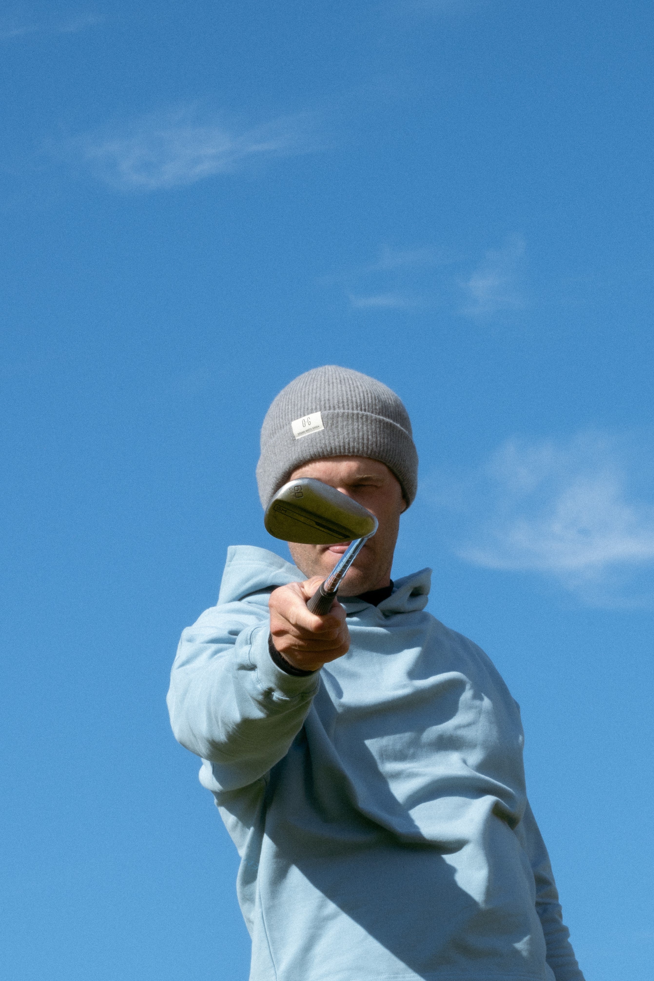 Ocean Meets Green Cloud beanie in grey, made from merino wool, worn by a male golfer pointing a club