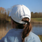 Ocean Meets Green Horizon cap in white with navy stitched logo, made from organic cotton, worn by a female golfer