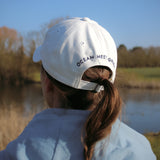 Ocean Meets Green Horizon cap in white with navy stitched logo, made from organic cotton, worn by a female golfer