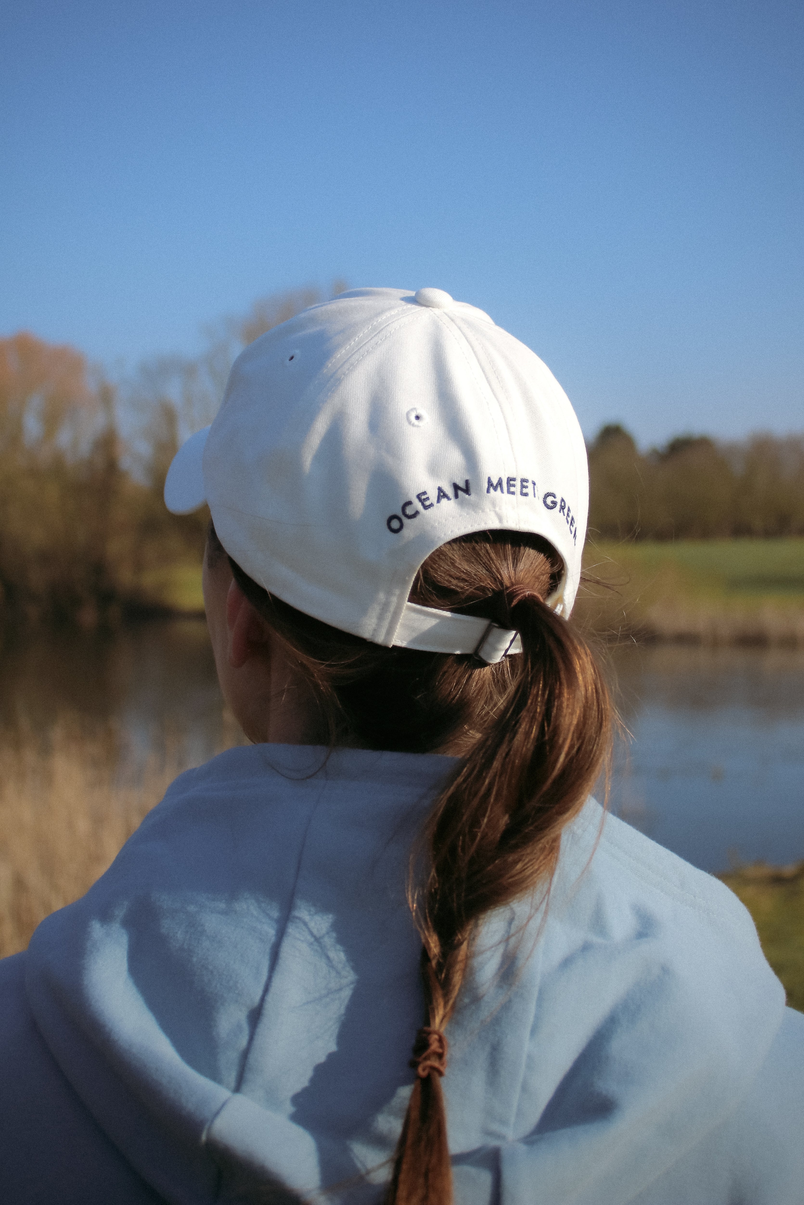 Ocean Meets Green Horizon cap in white with navy stitched logo, made from organic cotton, worn by a female golfer