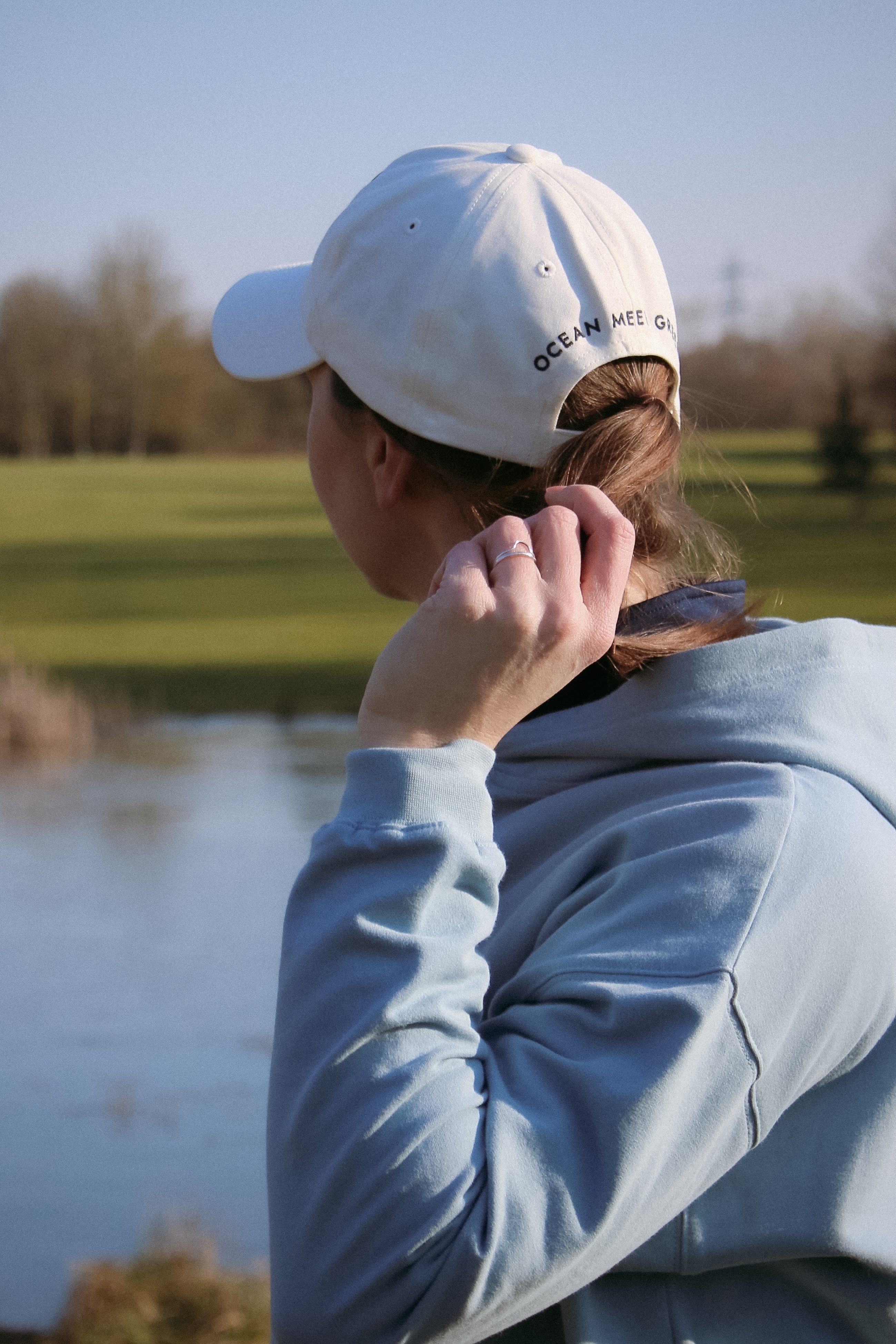 Ocean Meets Green Horizon cap in white with navy stitched logo, made from organic cotton, worn by a female golfer