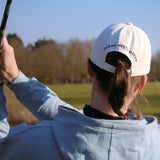 Ocean Meets Green Horizon cap in white with navy stitched logo, made from organic cotton, worn by a female golfer