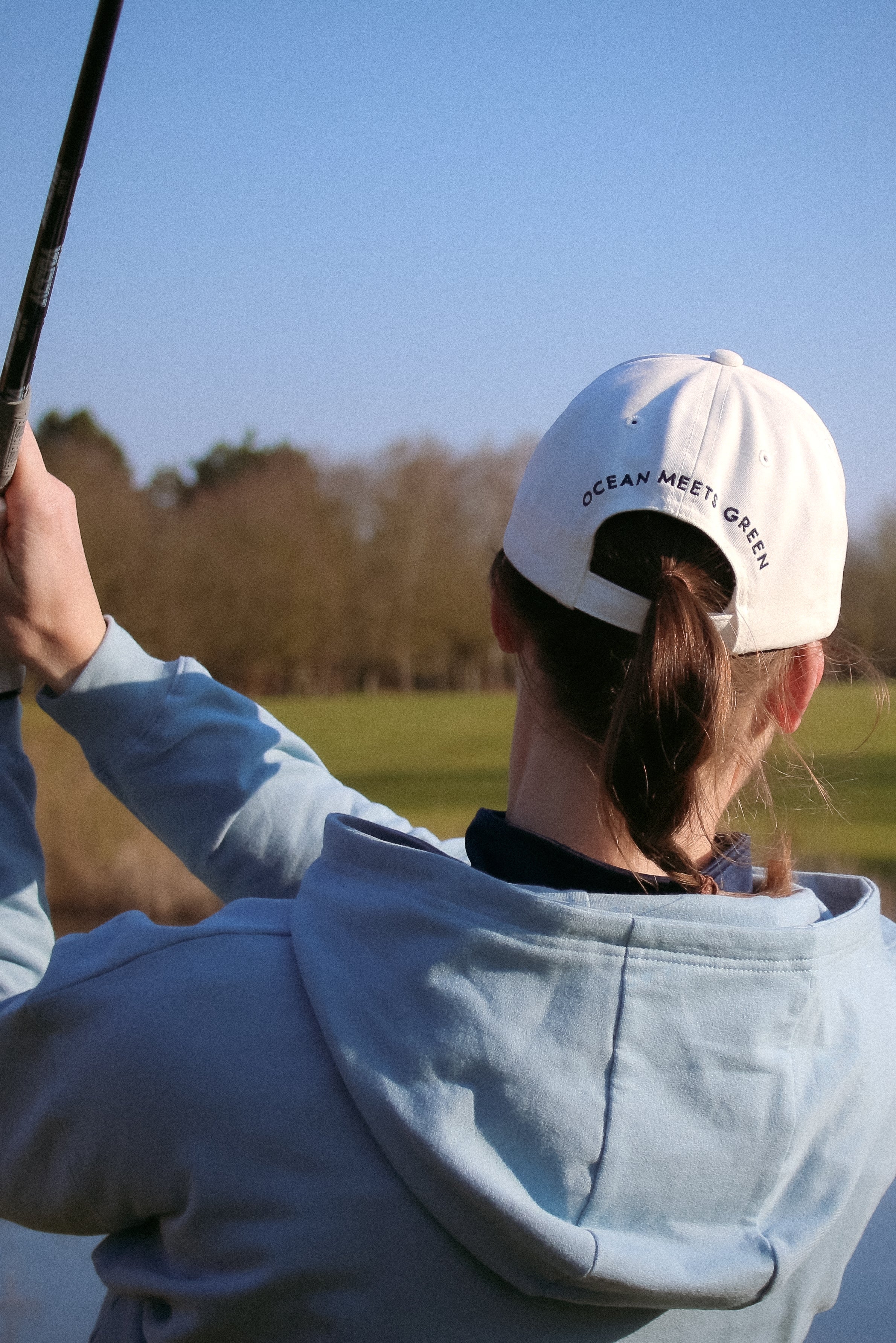 Ocean Meets Green Horizon cap in white with navy stitched logo, made from organic cotton, worn by a female golfer