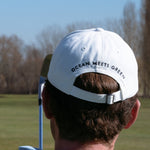 Ocean Meets Green Horizon cap in white with navy stitched logo, made from organic cotton, worn by a male golfer