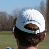 Ocean Meets Green Horizon cap in white with navy stitched logo, made from organic cotton, worn by a male golfer