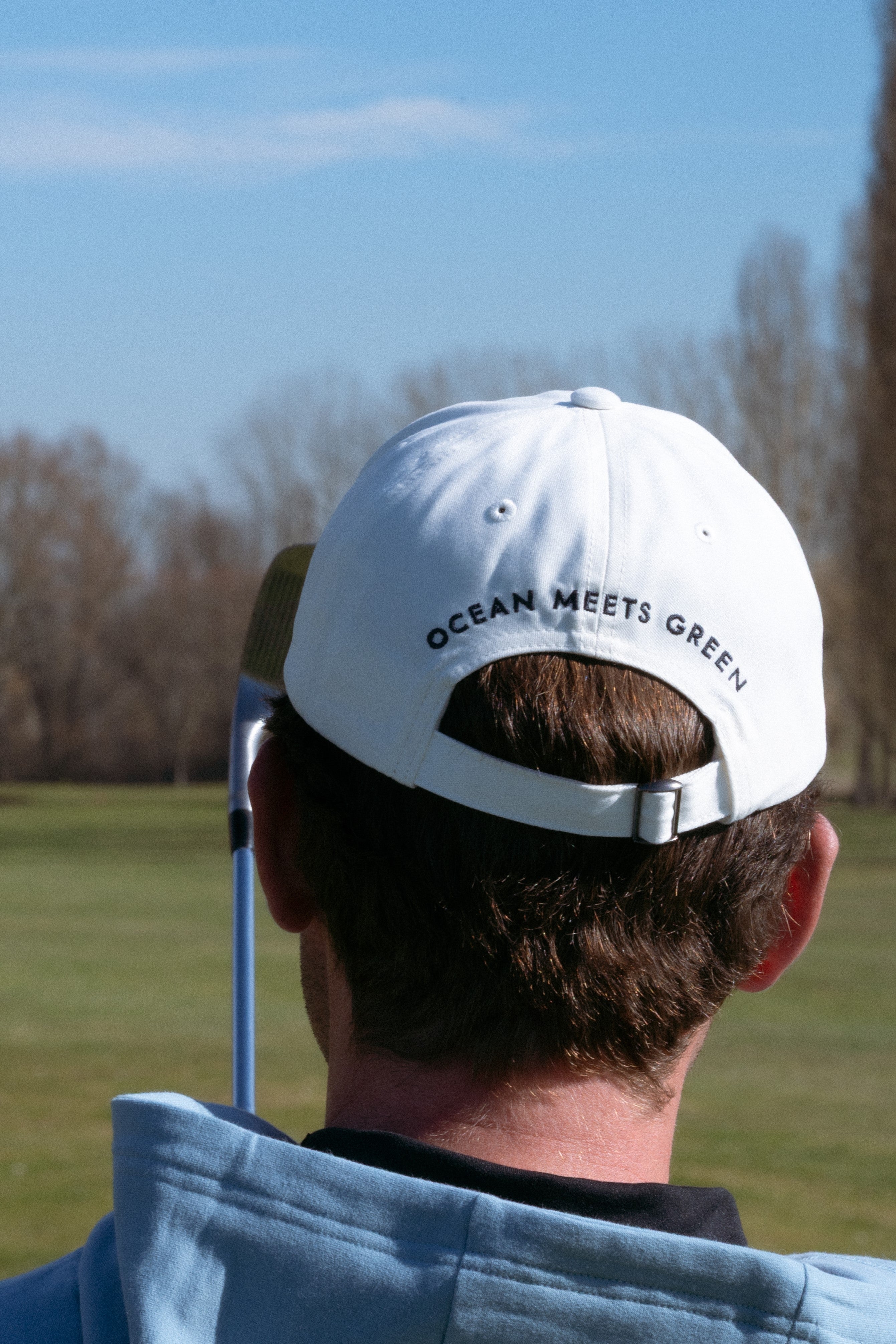 Ocean Meets Green Horizon cap in white with navy stitched logo, made from organic cotton, worn by a male golfer