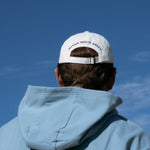 Ocean Meets Green Horizon cap in white with navy stitched logo, made from organic cotton, worn by a male golfer