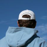 Ocean Meets Green Horizon cap in white with navy stitched logo, made from organic cotton, worn by a male golfer