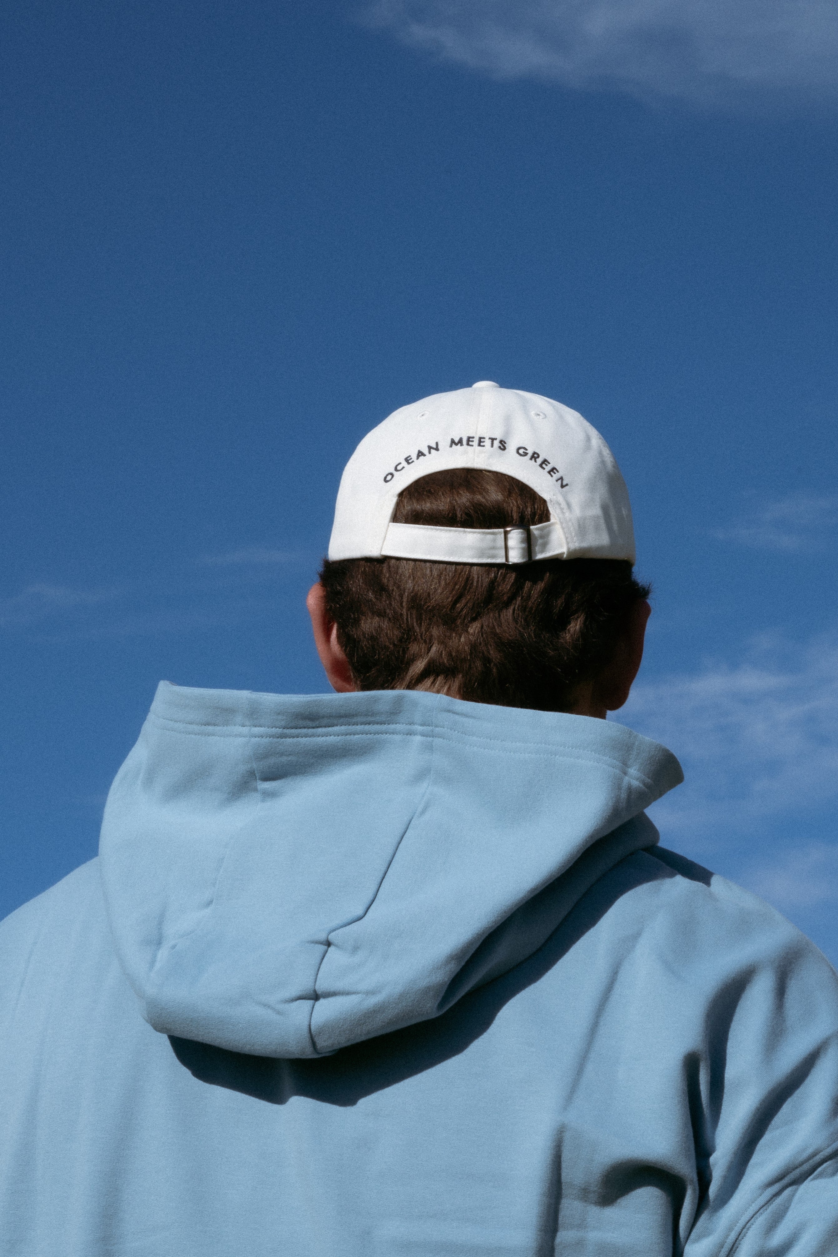 Ocean Meets Green Horizon cap in white with navy stitched logo, made from organic cotton, worn by a male golfer