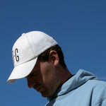 Ocean Meets Green Horizon cap in white with navy stitched logo, made from organic cotton, worn by a male golfer