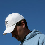 Ocean Meets Green Horizon cap in white with navy stitched logo, made from organic cotton, worn by a male golfer