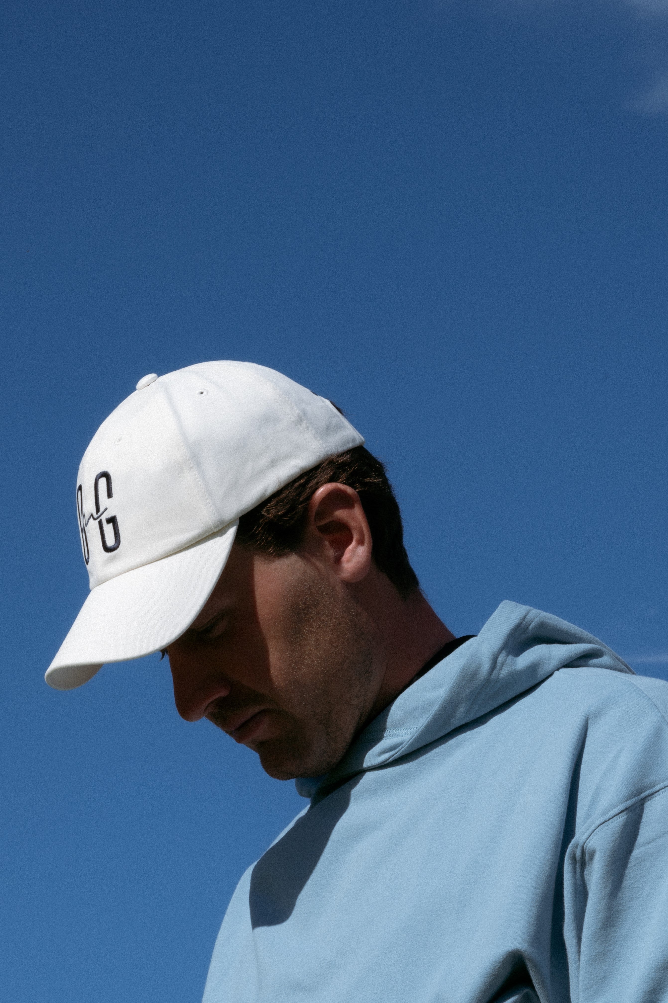 Ocean Meets Green Horizon cap in white with navy stitched logo, made from organic cotton, worn by a male golfer