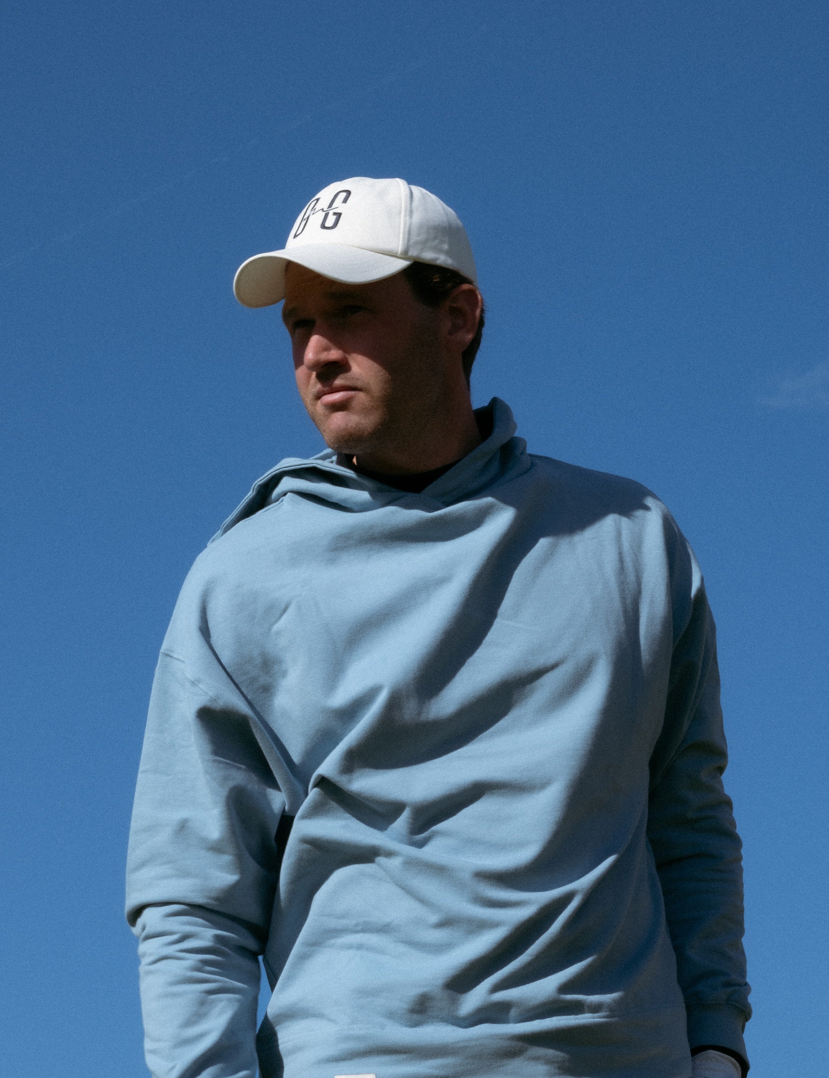 Ocean Meets Green Horizon cap in white with navy stitched logo, made from organic cotton, worn by a male golfer
