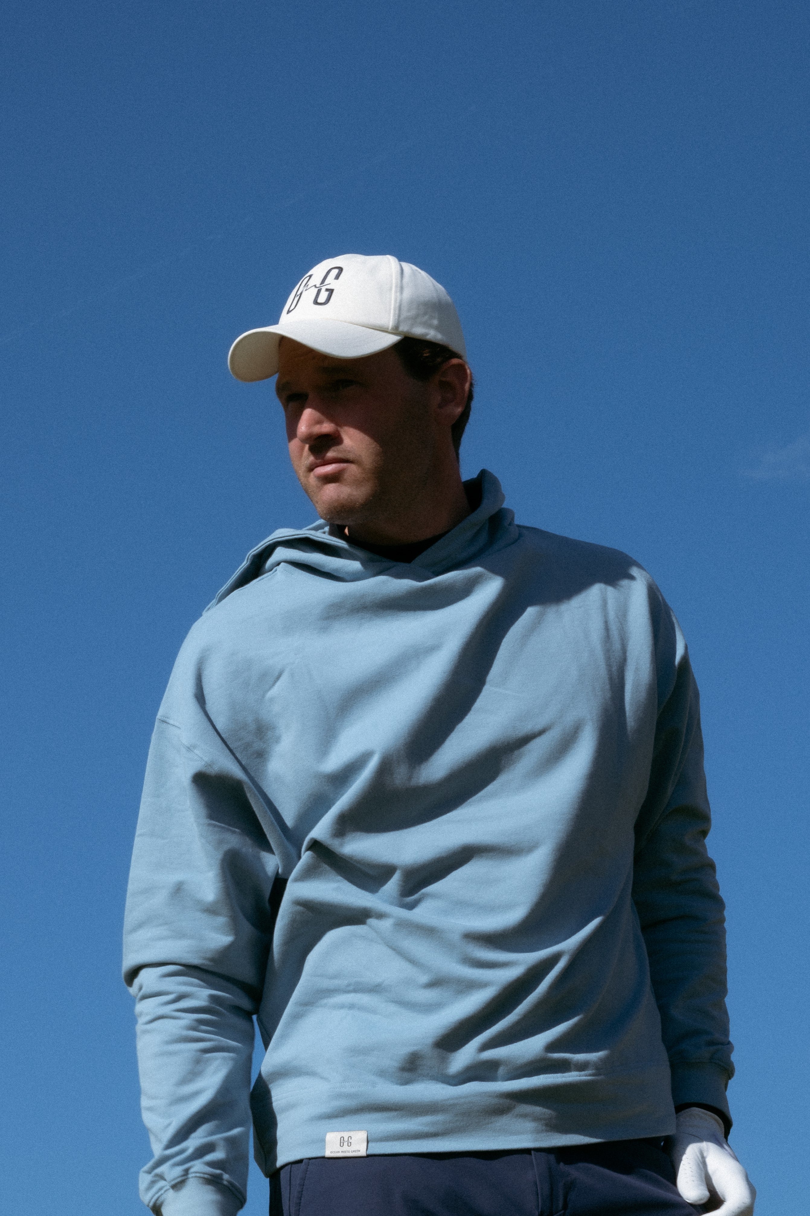 Ocean Meets Green Horizon cap in white with navy stitched logo, made from organic cotton, worn by a male golfer
