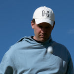 Ocean Meets Green Horizon cap in white with navy stitched logo, made from organic cotton, worn by a male golfer