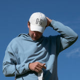 Ocean Meets Green Horizon cap in white with navy stitched logo, made from organic cotton, worn by a male golfer