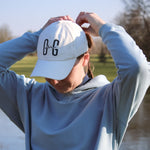 Ocean Meets Green Horizon cap in white with navy stitched logo, made from organic cotton, worn by a female golfer