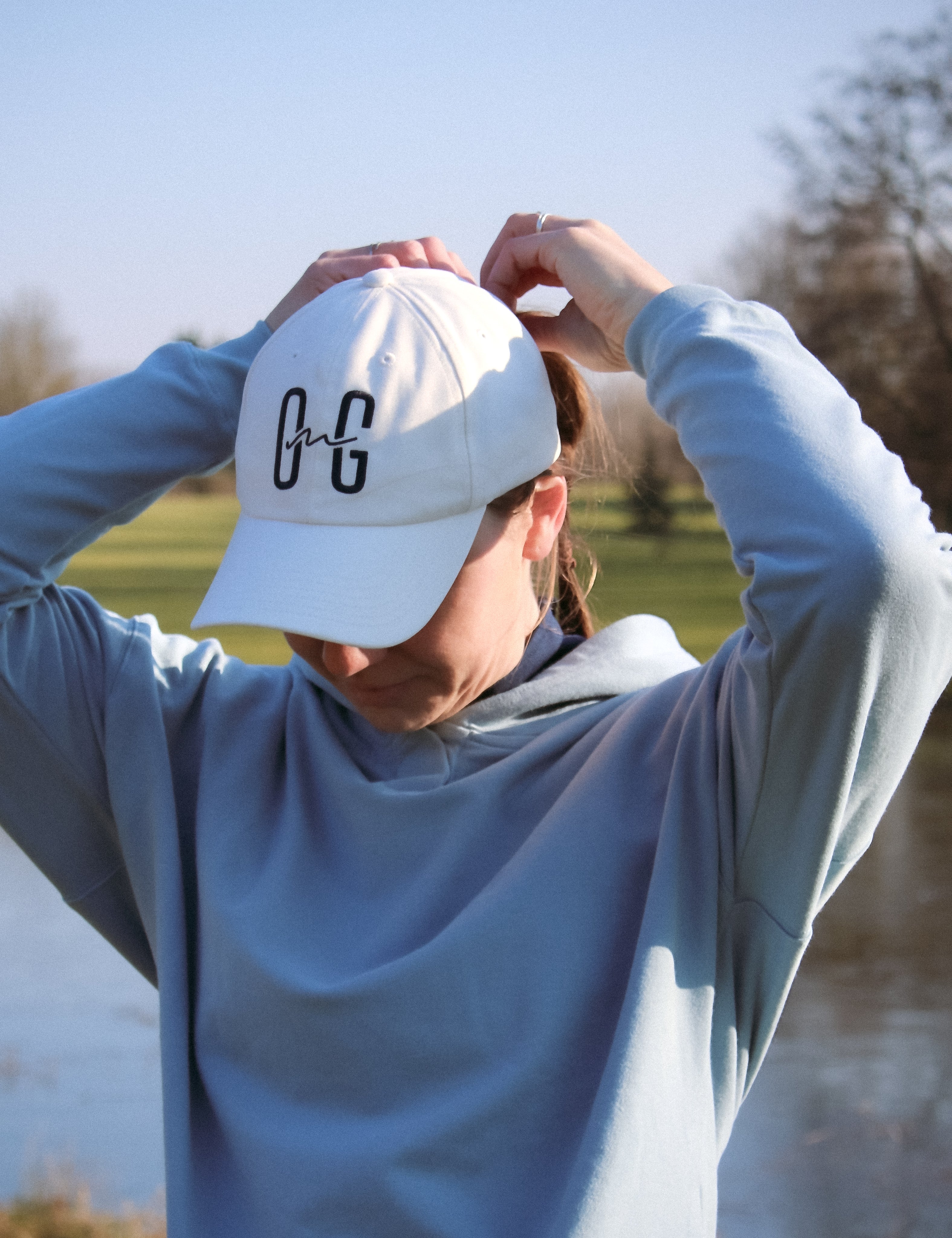 Ocean Meets Green Horizon cap in white with navy stitched logo, made from organic cotton, worn by a female golfer