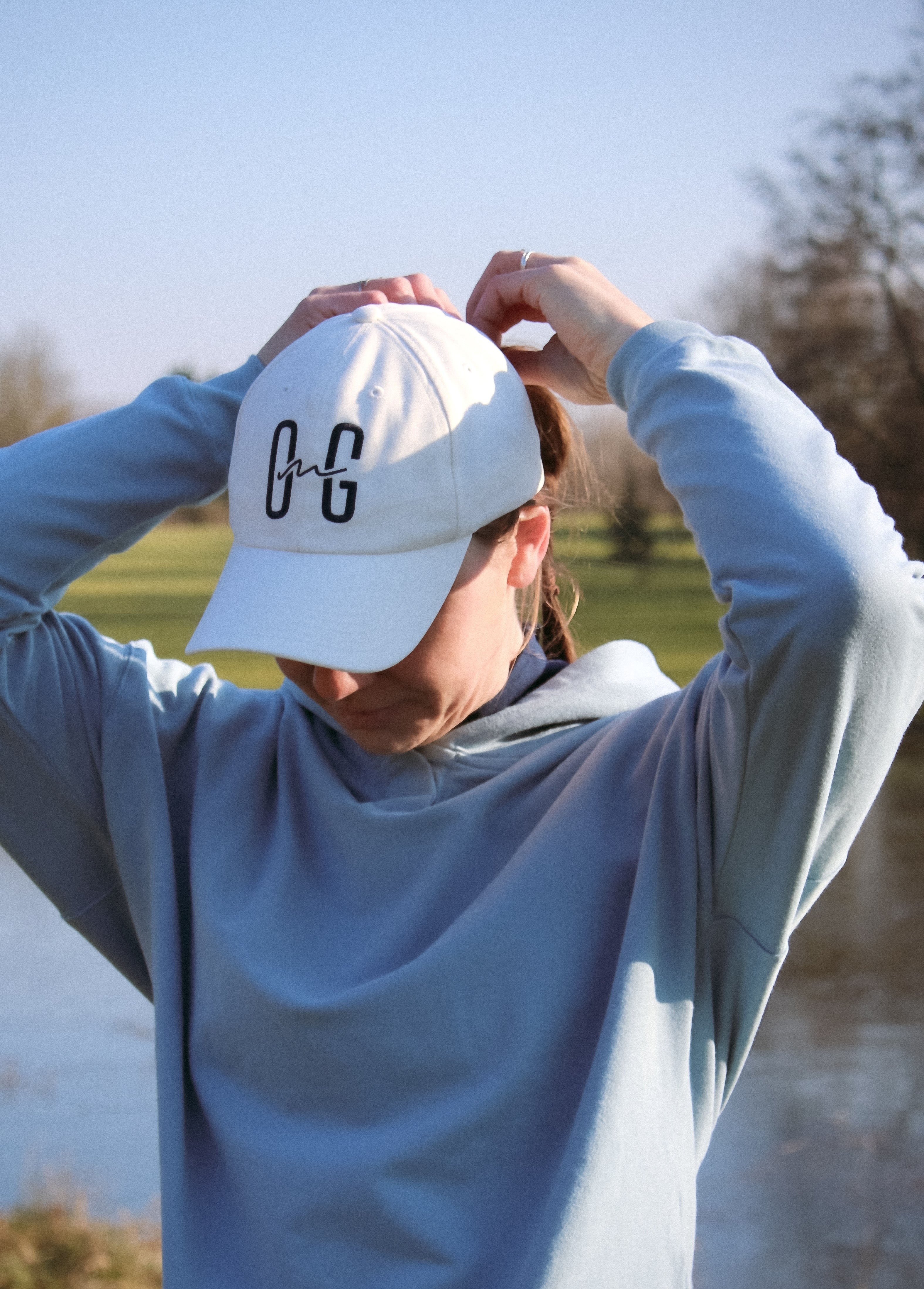 Ocean Meets Green Horizon cap in white with navy stitched logo, made from organic cotton, worn by a female golfer