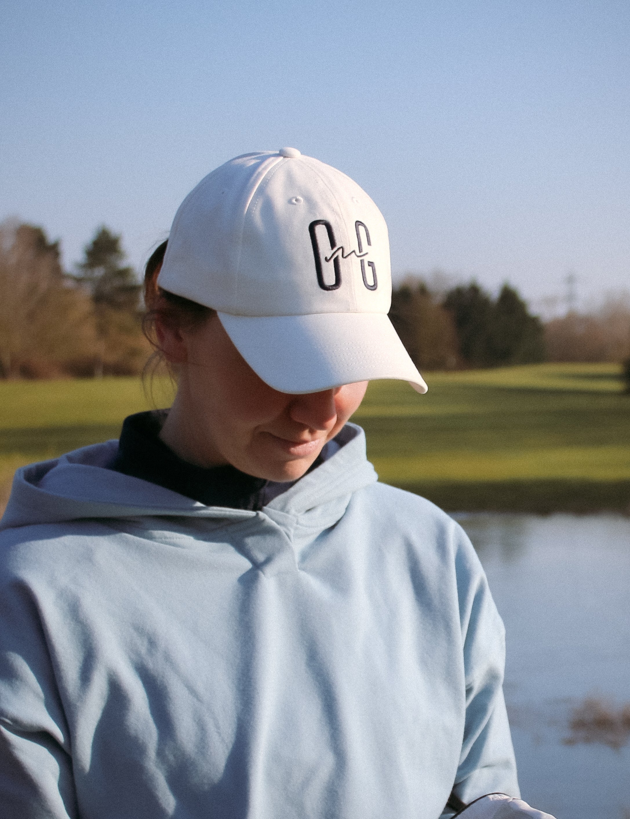 Ocean Meets Green Horizon cap in white with navy stitched logo, made from organic cotton, worn by a female golfer