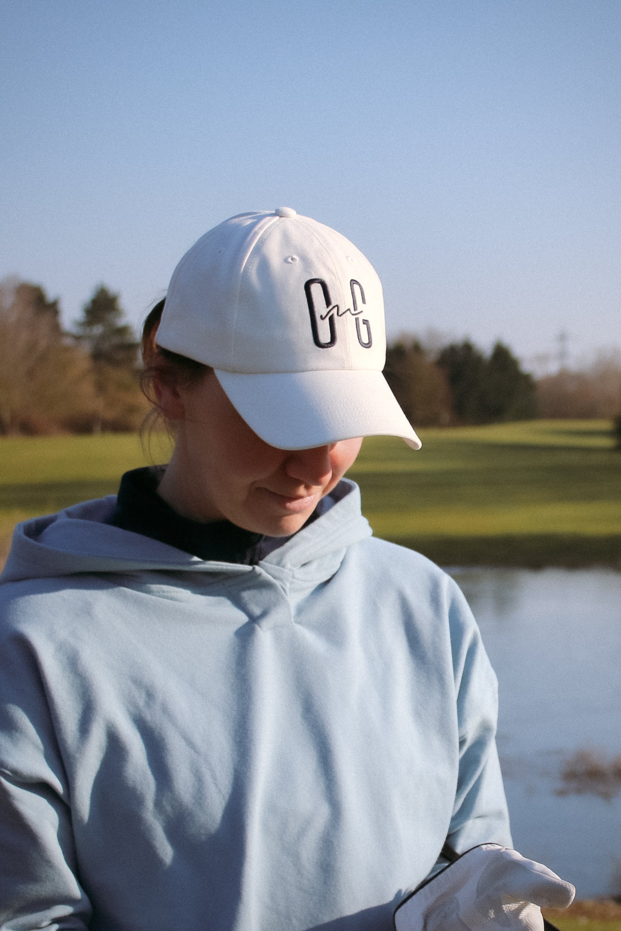 Ocean Meets Green Horizon cap in white with navy stitched logo, made from organic cotton, worn by a female golfer