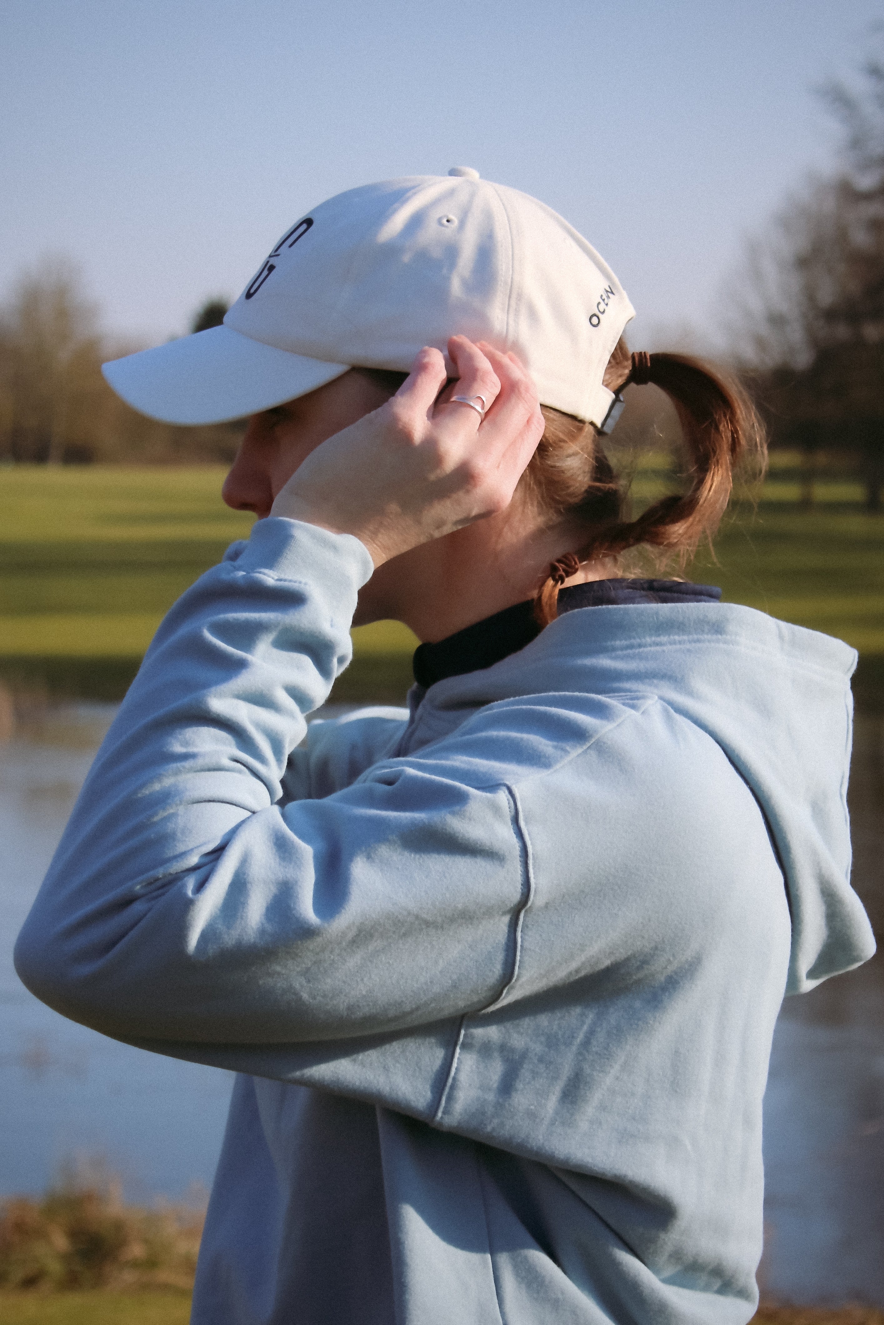 Ocean Meets Green Horizon cap in white with navy stitched logo, made from organic cotton, worn by a female golfer