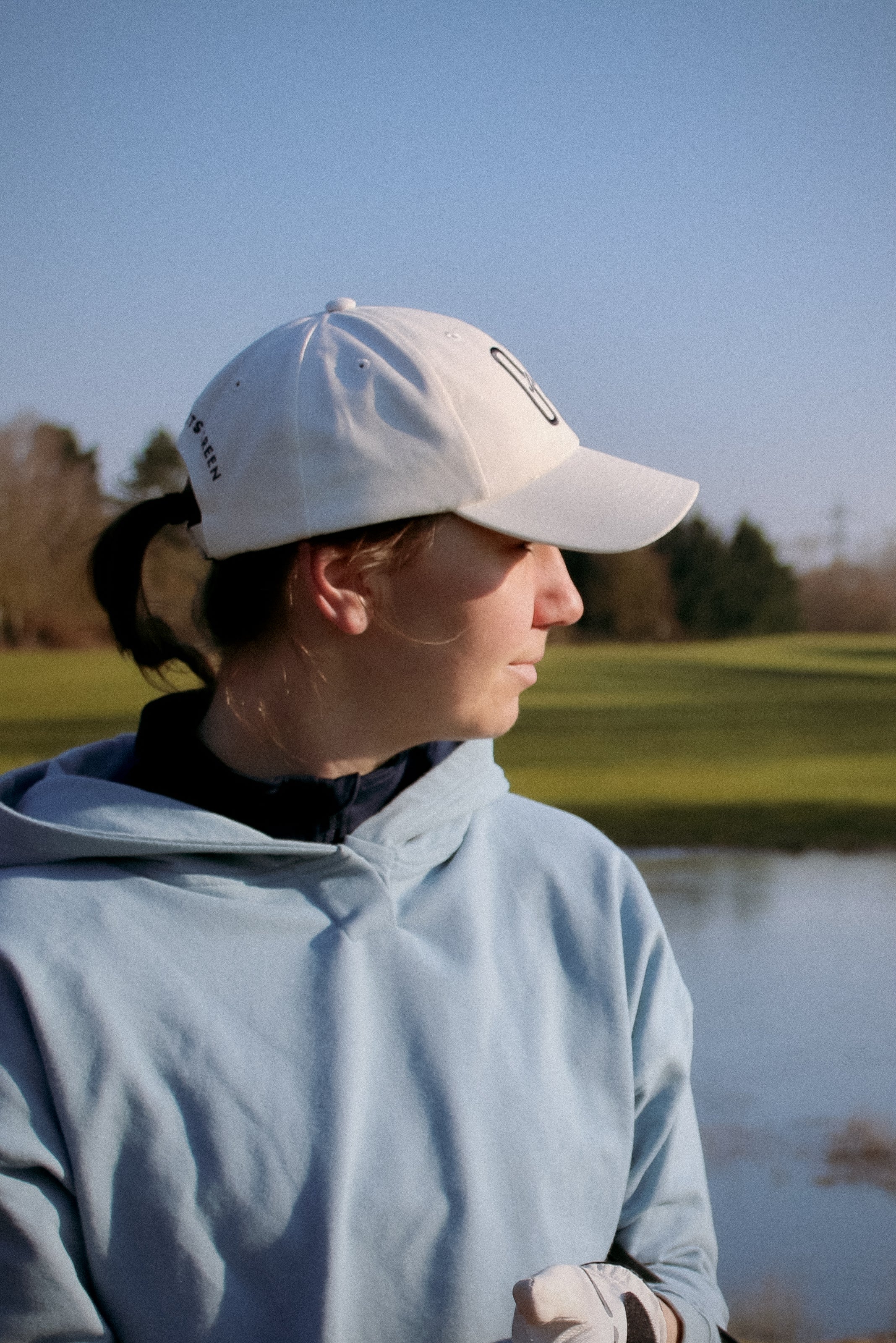 Ocean Meets Green Horizon cap in white with navy stitched logo, made from organic cotton, worn by a female golfer