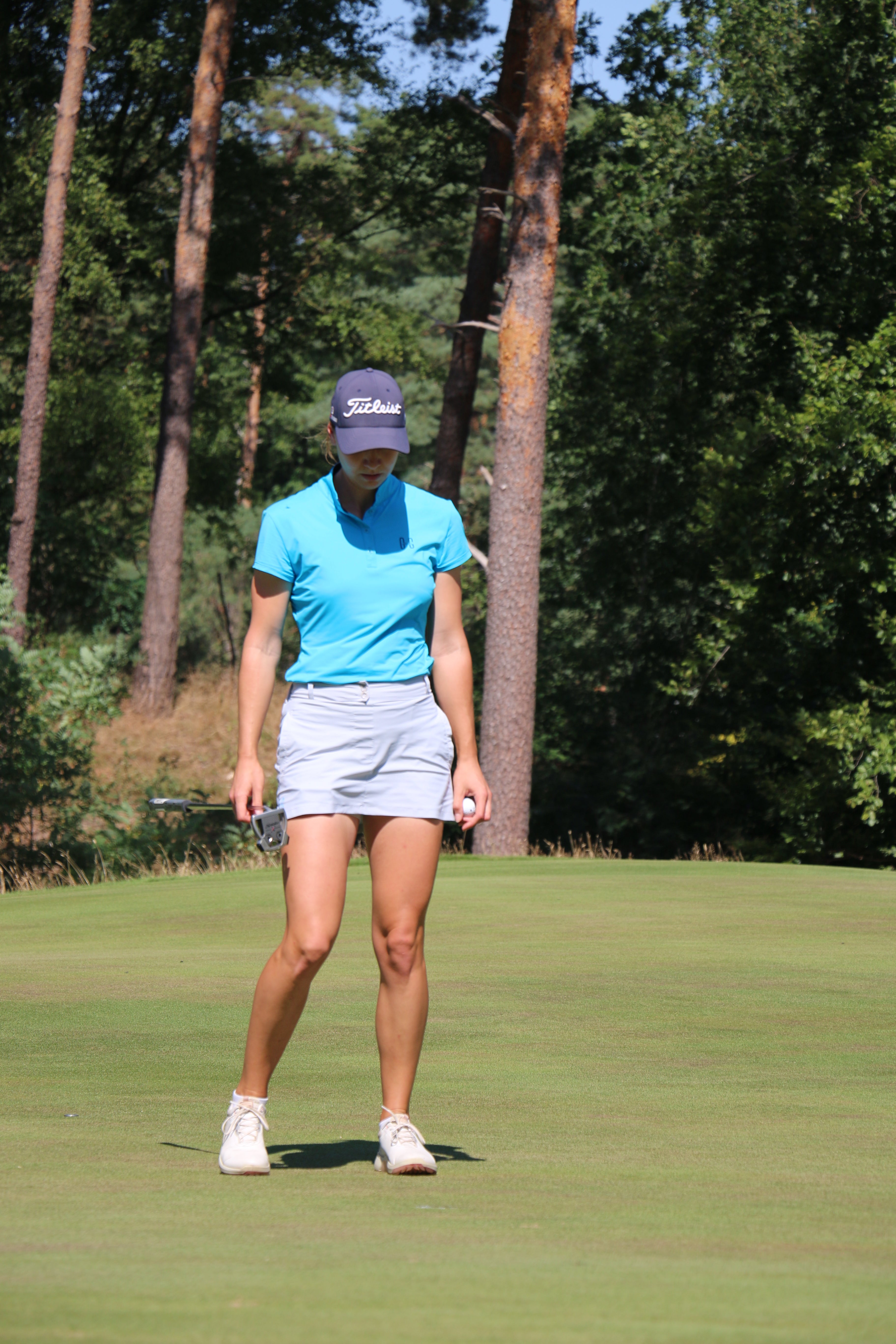 Image of female golfer wearing the Ocean Meets Green TIDE skirt in grey and the MOANA poloshirt in light blue