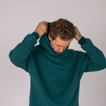 Full body image of Ocean Meets Green men's golf hoodie Wave in pine, pulling the hood over the head