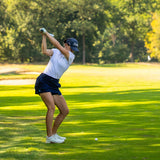 Image of female golfer wearing the Ocean Meets Green TIDE skirt in navy and the MOANA poloshirt in white