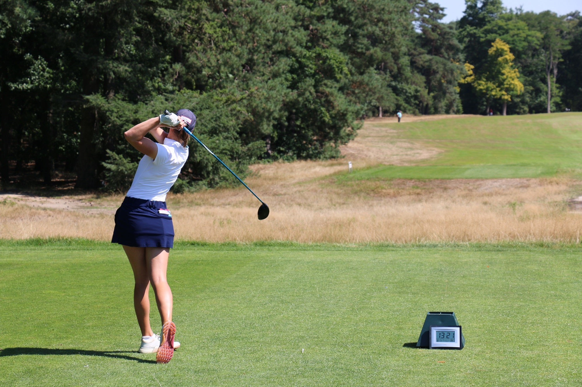 Image of female golfer wearing the Ocean Meets Green TIDE skirt in navy and the MOANA poloshirt in white