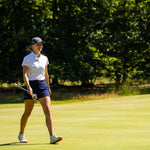 Image of female golfer wearing the Ocean Meets Green TIDE skirt in navy and the MOANA poloshirt in white