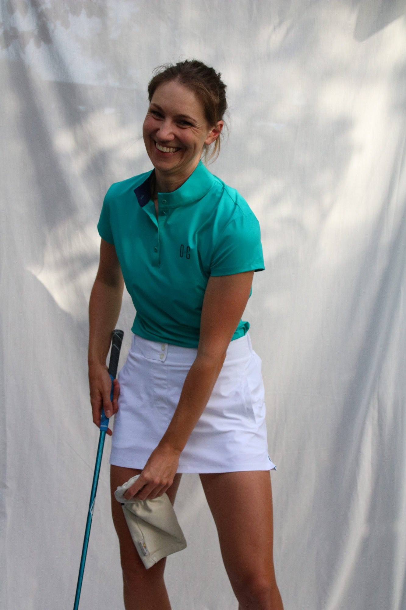 Image of woman wearing Ocean Meets Green Moana golf polo in green and Tide skirt in white